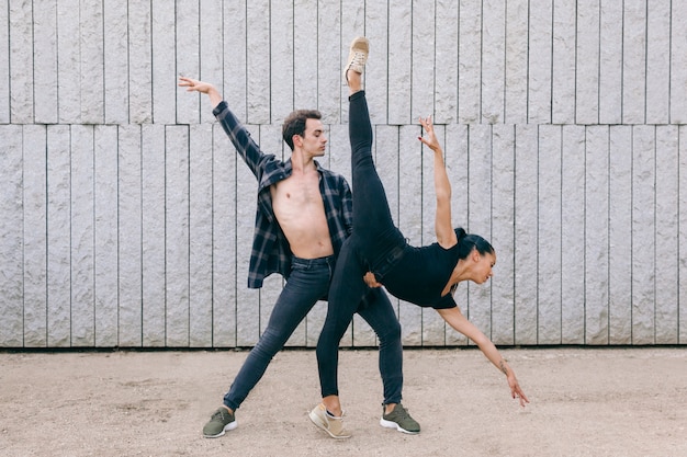 Casal de dançarinos masculinos e femininos, realizando uma pose de balé com roupas casuais