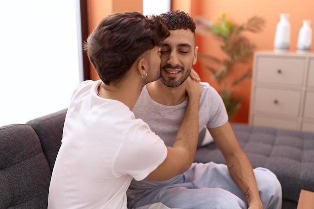 Casal de dois homens hispânicos sentados no sofá se abraçando e se beijando em casa