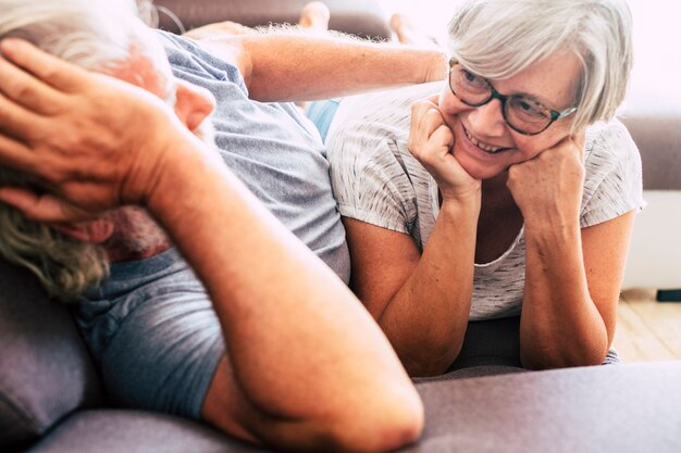 Casal de dois idosos em um relacionamento e casados deitados no sofá juntos - mulher olhando para o homem sorrindo - amor e carinho