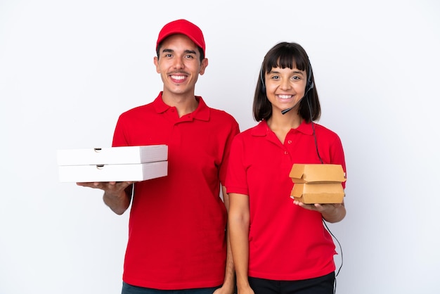 Casal de entrega jovem segurando pizzas e hambúrgueres isolados no fundo branco posando com os braços no quadril e sorrindo