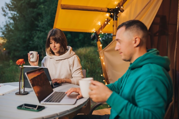 Casal de família feliz freelancers trabalhando laptop em uma barraca de glamping aconchegante na noite de verão Barraca de acampamento de luxo para férias ao ar livre e férias Conceito de estilo de vida