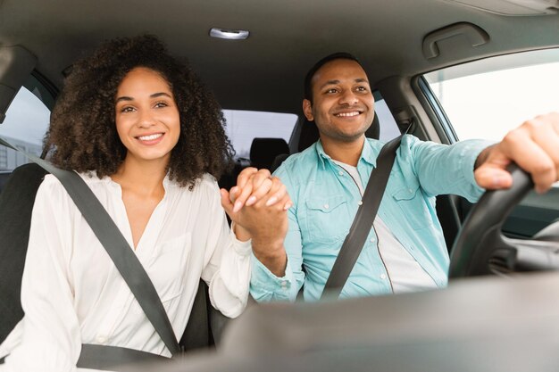 Casal de família negra de mãos dadas sentado no carro curtindo o passeio