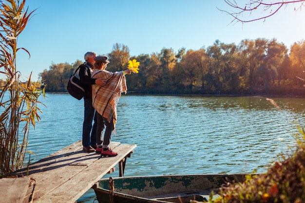 Foto casal de família sênior andando pelo lago de outono. feliz homem e mulher, curtindo a natureza e abraçando no cais