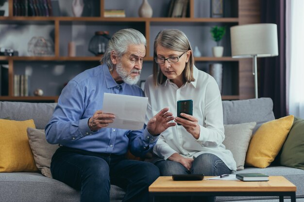 Casal de família sênior homem e mulher de cabelos grisalhos pagam por serviços inserem documentos de dados usando aplicativo smartphone móvel Aposentados em casa cheques de contas de serviços públicos usam telefone inteligente de computador