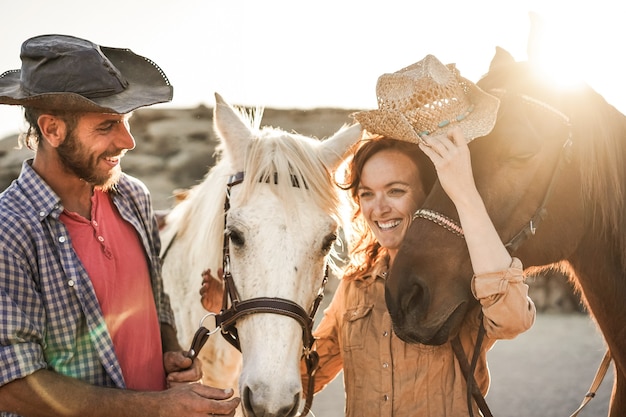 Casal de fazendeiros se divertindo com cavalos sem bits durante o dia de sol dentro do curral do rancho - foco principal no cavalo certo