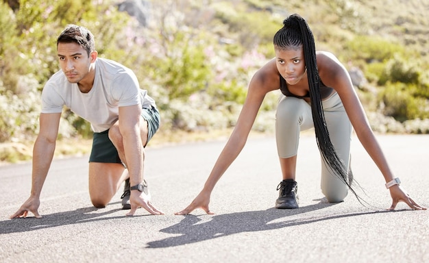 Casal de fitness de corrida esportiva e pronto para correr estrada de asfalto com ajuste competitivo e corredores ativos para treino ao ar livre Homem asiático e mulher negra sentados em posição para iniciar o treinamento de atletas de corrida