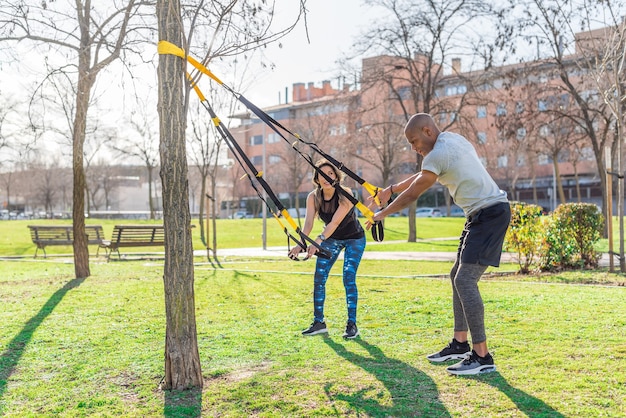 Casal de fitness fazendo exercícios de braços com alças trx fitness no parque. Pessoas multiétnicas fazendo exercícios ao ar livre.