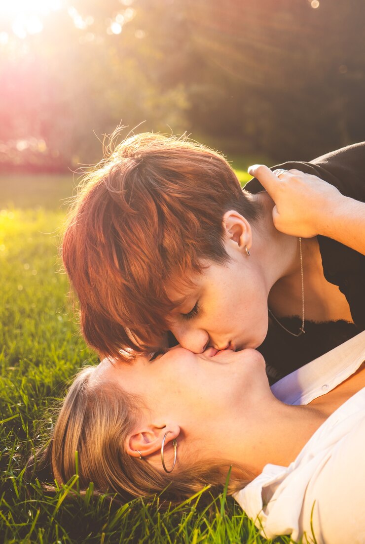 Foto casal de garotas apaixonadas se beijando deitada na grama em um parque em um dia ensolarado