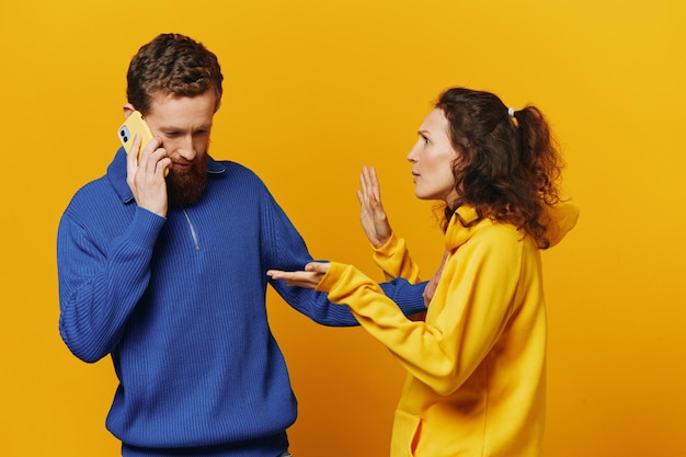 Casal de homem e mulher com telefone na mão ligam falando ao telefone em um fundo amarelo símbolos sinais e gestos com as mãos briga familiar ciúme e escândalo