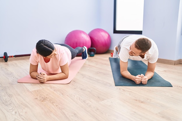 Casal de homem e mulher sorrindo confiante treinando exercícios abdominais no centro esportivo