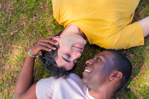 Casal de homens multiétnicos em um conceito de parque lgbt deitado na grama em uma pose romântica