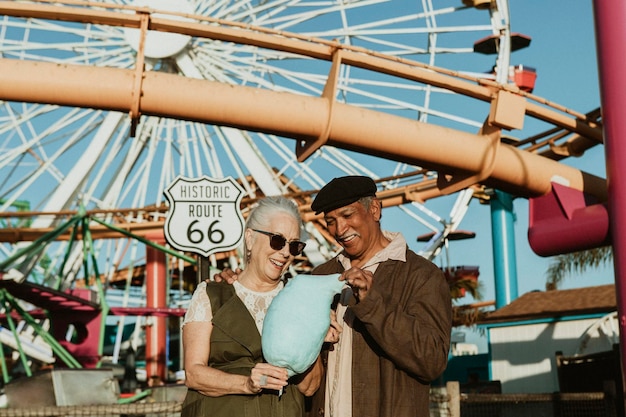 Foto casal de idosos alegres apreciando algodão doce no pacific park em santa monica, califórnia