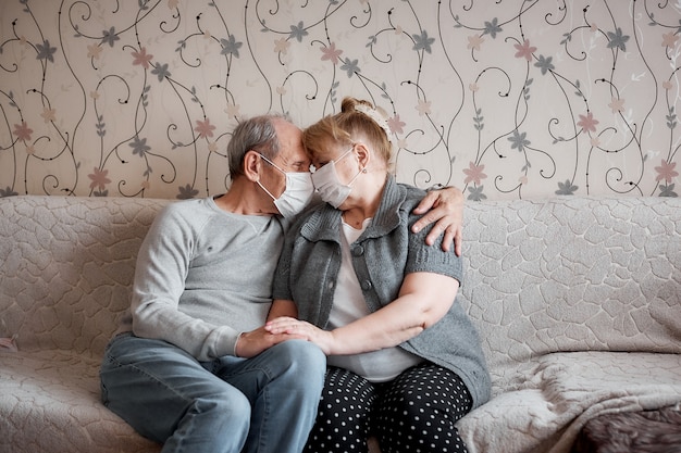 Casal de idosos apaixonados em máscaras médicas em casa em quarentena, valores familiares