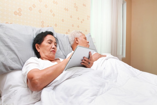 Foto casal de idosos asiáticos deitado na cama no quarto mulher idosa insônia olhe para mídia social on-line conceito de família cuidados de saúde seguro de saúde para idosos