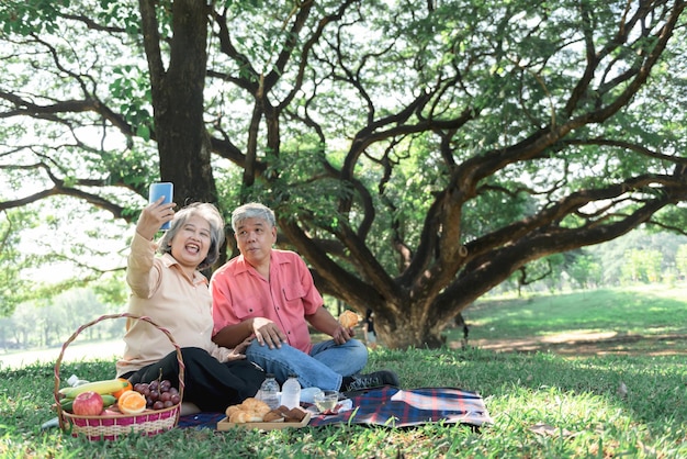 Casal de idosos asiáticos passou feliz juntos relaxando no jardim usando telefone celular para tirar uma foto