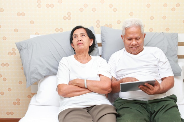 Casal de idosos deitado na cama Esposa insatisfeita com marido jogando tablet Conceitos familiares cuidados de saúde para idosos em idade de aposentadoria