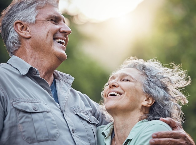 Casal de idosos e abraço com sorriso na natureza romance juntos para aproveitar o ar das árvores e o sol Homem sênior mulher e amor na aposentadoria rindo do lado de fora mostram felicidade, cuidado e união em momentos de diversão