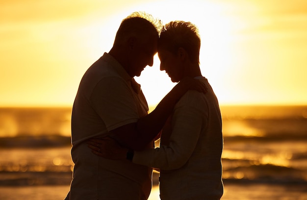 Casal de idosos e silhueta na praia com abraço na noite do pôr do sol ou entardecer por ondas de água ou horizonte juntos Homem e mulher sênior no oceano, mar ou sol para carinho, carinho ou amor no romance