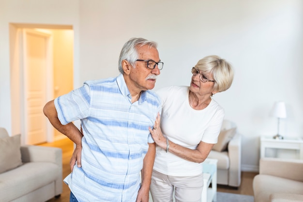 Casal de idosos em casa. O homem idoso está tendo dores nas costas e sua linda esposa o apóia.