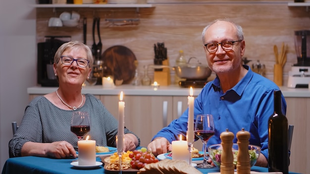 Casal de idosos fazendo uma videochamada na cozinha durante um jantar romântico, comendo uma refeição festiva. Pov online internet conferência moderna, bate-papo, comunicação, bate-papo, conversa, chamada via webcam