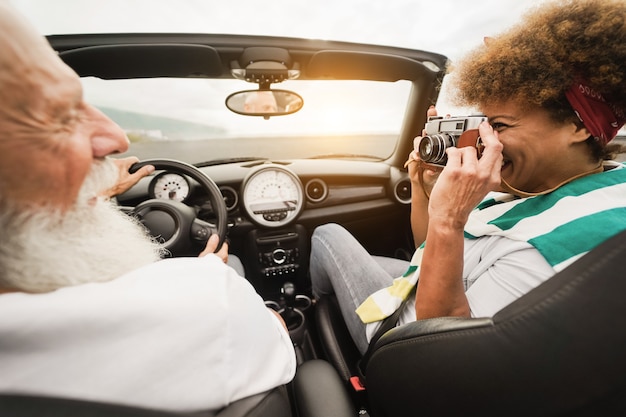 Casal de idosos feliz se divertindo em um carro conversível durante as férias de verão - foco principal na câmera vintage