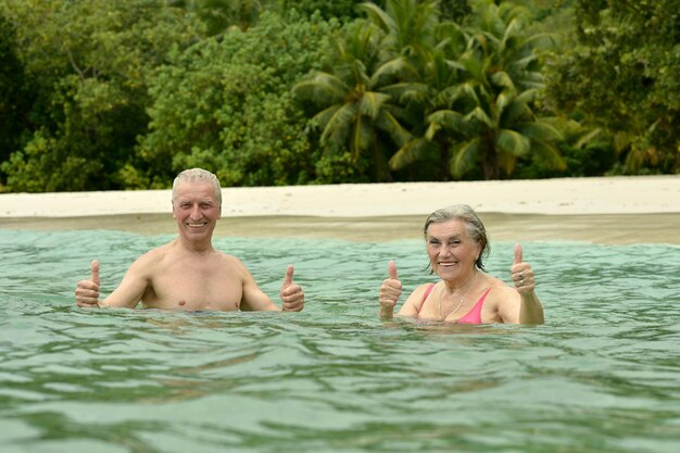 Casal de idosos felizes descansando em uma praia tropical com as mãos ao alto