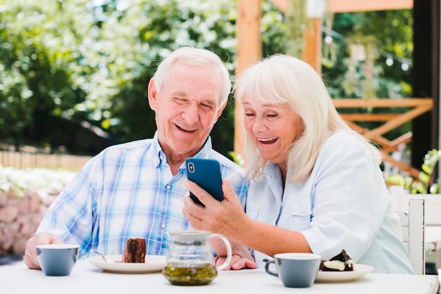 Casal de idosos rindo olhando para smartphone