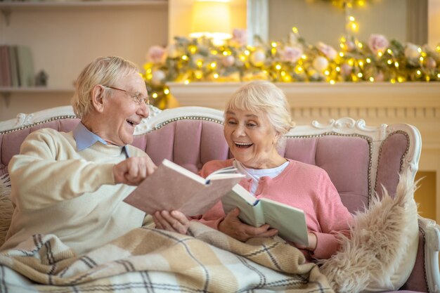 Casal de idosos sentado em um sofá lendo livros