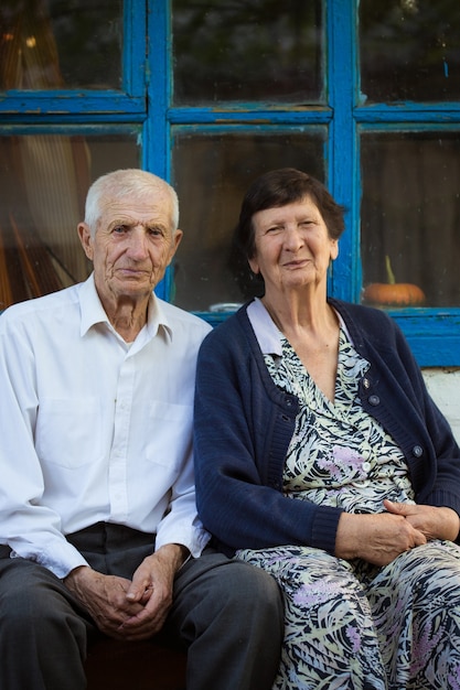 Casal de idosos sentado na frente de uma casa rural