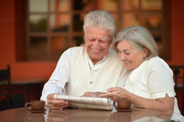 Casal de idosos tomando chá e lendo jornal ao ar livre em um café