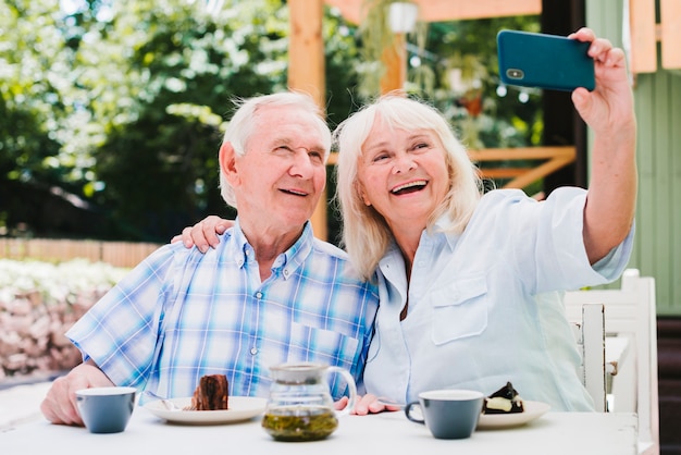 Foto casal de idosos tomando selfie sorrindo sentado no terraço exterior