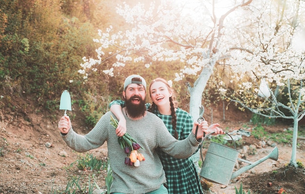 Casal de jardineiro engraçado segurando ferramentas de jardim nas plantas de fundo da natureza da primavera e jardinagem como sprin