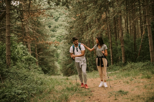 Casal de jovens caminhantes com mochilas caminham pela floresta