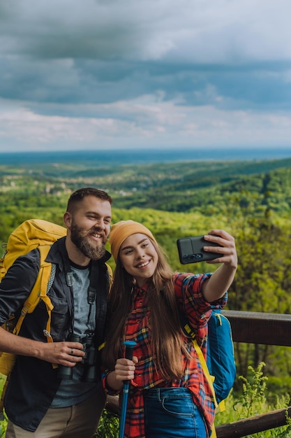 Casal de jovens caminhantes tomando selfie com um smartphone enquanto usava mochilas de acampamento