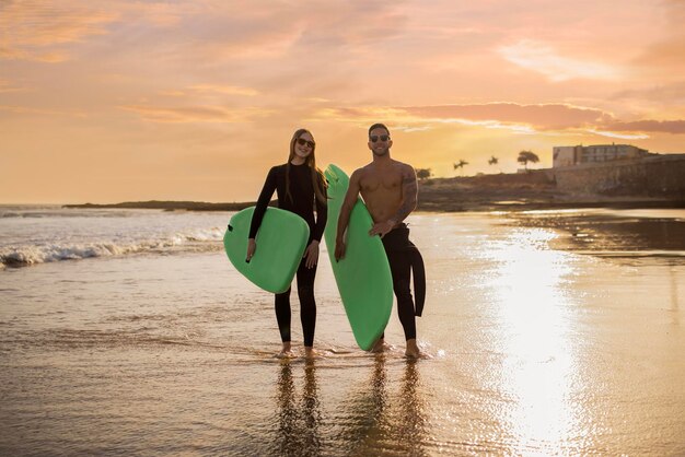 Casal de jovens surfistas com pranchas de surf andando na praia na hora do pôr do sol