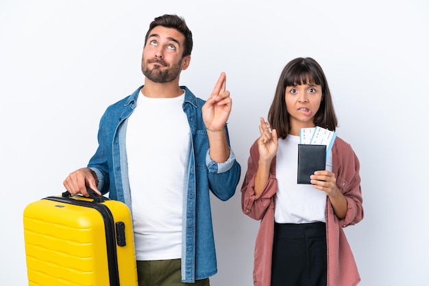 Casal de jovens viajantes segurando uma mala e um passaporte isolado no fundo branco com os dedos se cruzando e desejando o melhor