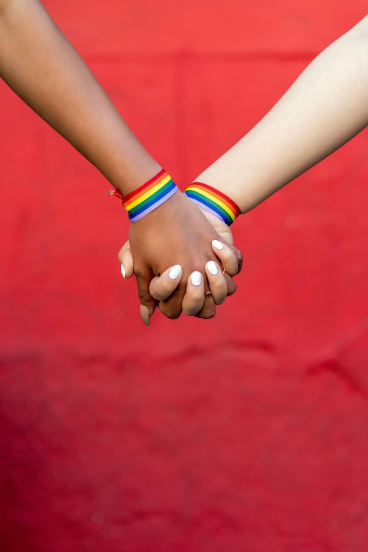 Foto casal de lésbicas de mãos dadas com pulseira do orgulho gay