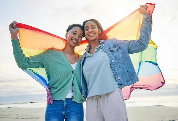 Casal de lésbicas e bandeira do orgulho na praia juntos em felicidade pela comunidade LGBTQ ou direitos Retrato de mulheres gays ou bissexuais orgulhosas e confiantes sorriem na costa do oceano em amor, apoio ou confiança