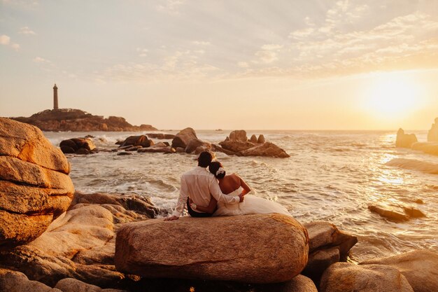 Casal de lua de mel relaxa na praia do pôr do sol Vista para o mar com farol