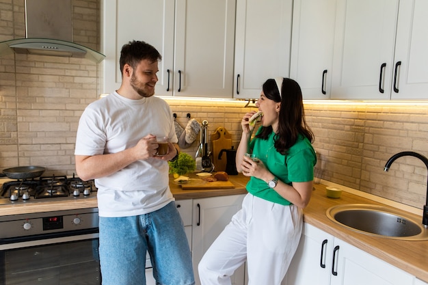 Casal de manhã na cozinha tomando café da manhã, navegando na internet no telefone, copie o espaço