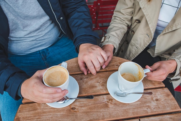 Foto casal de mãos dadas enquanto bebe café com leite no café ao ar livre
