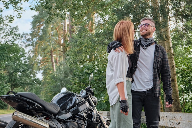 Casal de meia idade abraçando e se divertindo em uma motocicleta viajando juntos em uma estrada florestal