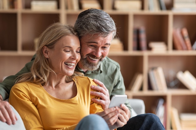Casal de meia idade feliz assistindo fotos de família no smartphone em casa