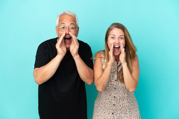 Casal de meia-idade isolado em um fundo azul gritando e anunciando algo