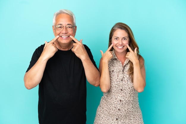 Casal de meia-idade isolado em um fundo azul sorrindo com uma expressão feliz e agradável