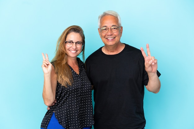 Casal de meia-idade isolado em um fundo azul sorrindo e mostrando sinal de vitória