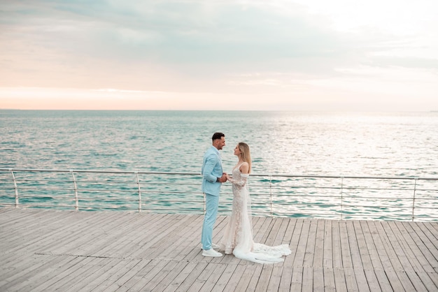 Foto casal de moda jovem de mãos dadas na ponte de madeira no fundo do mar e céu azul