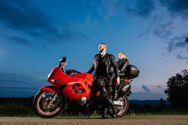 Casal de motoqueiros legal em jaquetas de couro sentado na bicicleta esportiva vermelha ao ar livre