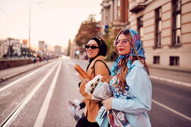 Casal de mulheres, uma usando um hijab e um vestido moderno e tradicional e a outra com um vestido azul