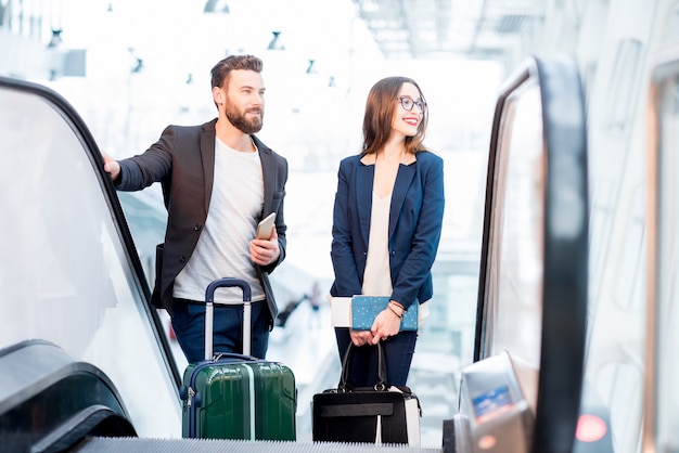 Casal de negócios elegante com bagagem subindo na escada rolante para a área de embarque do aeroporto